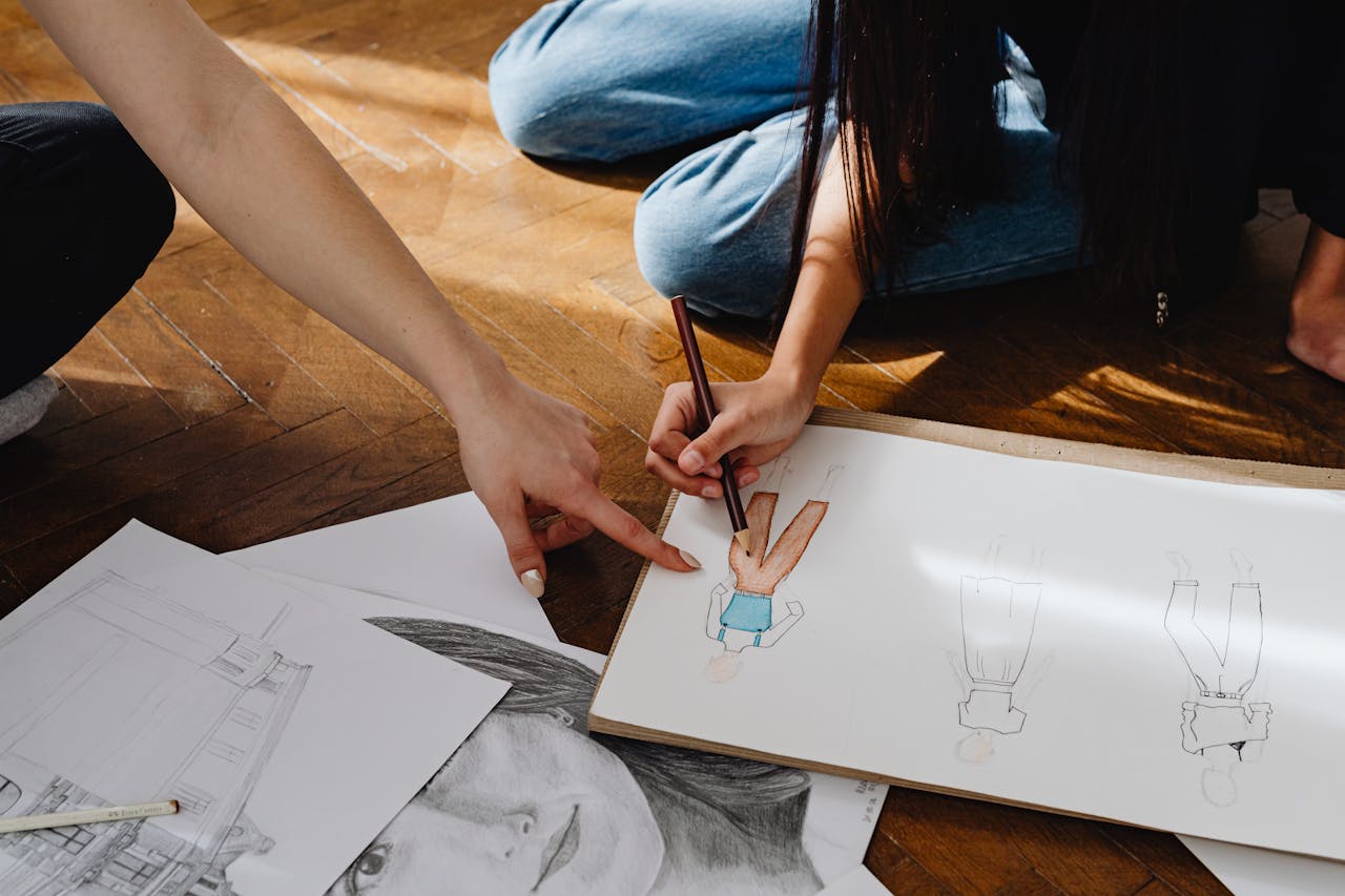 Close-up of hands sketching fashion designs on paper indoors.