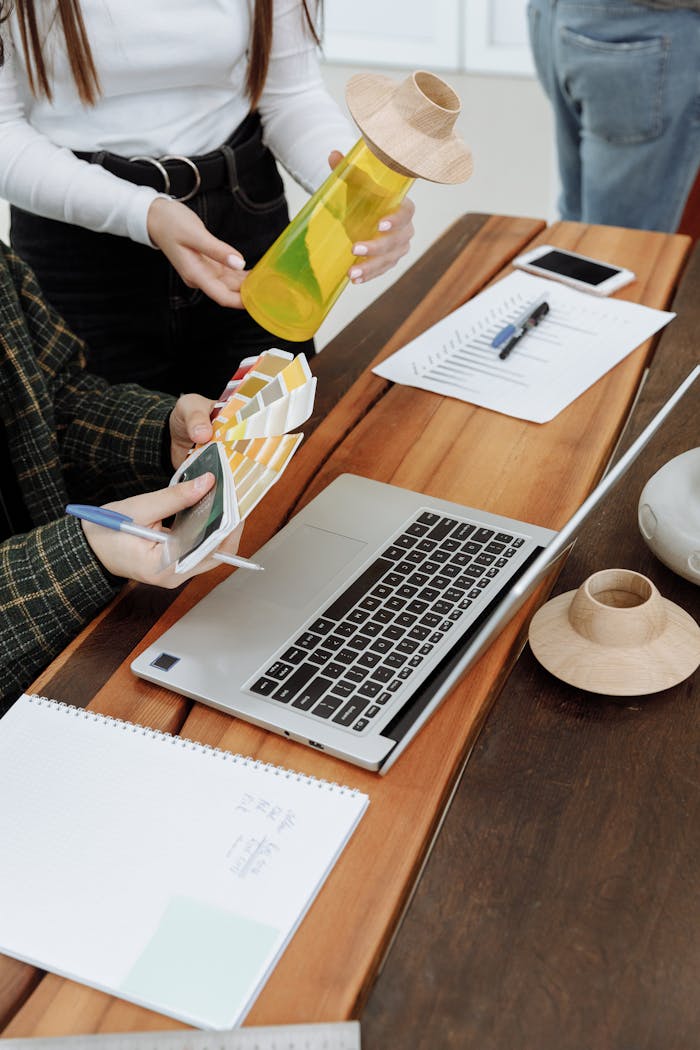 Designers working with color swatches, a laptop, and creative tools at a wooden table.